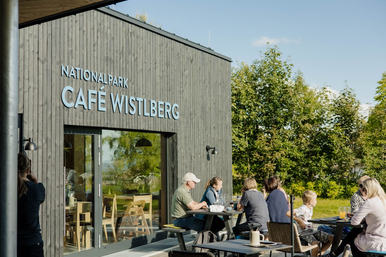 Gäste sitzen bei sonnigem Wetter auf der Terrasse des Nationalpark Café Wistlberg und genießen kühle Getränke im Freien.