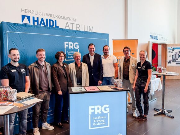 Acht Personen stehen an einem Informationsstand der Ausbildungs- und Arbeitsbörse im HAIDL-Atrium in Röhrnbach, umgeben von FRG-Schildern.