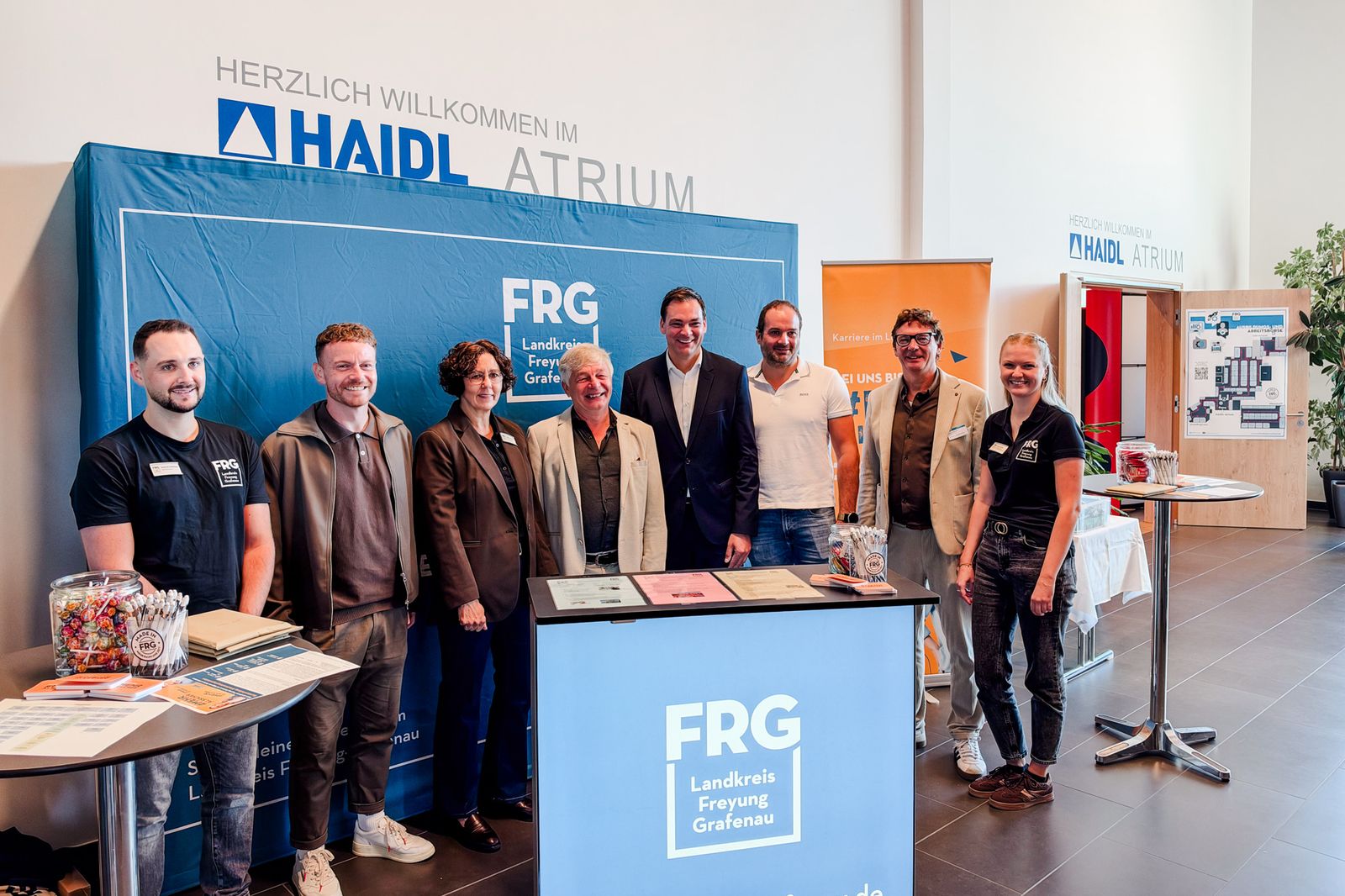 Acht Personen stehen an einem Informationsstand der Ausbildungs- und Arbeitsbörse im HAIDL-Atrium in Röhrnbach, umgeben von FRG-Schildern.