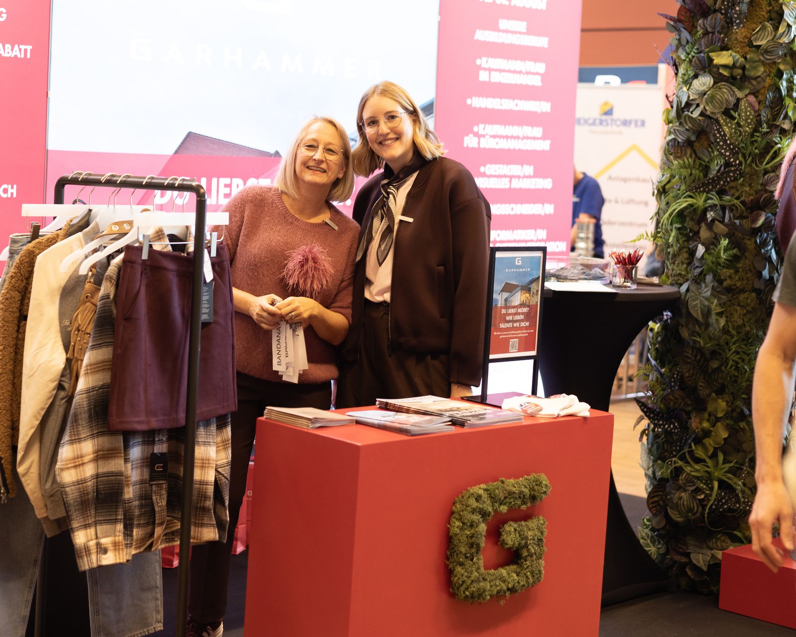 Zwei Mitarbeiterinnen präsentieren Mode und Ausbildungsinformationen am GARHAMMER-Stand der AuA 2025 in Freyung-Grafenau.