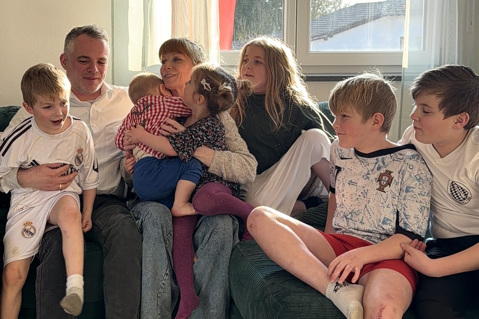 Steffi und Martin Dorsch sitzen mit ihren sieben Kindern auf dem Sofa in ihrem neuen Zuhause in Freyung-Grafenau.