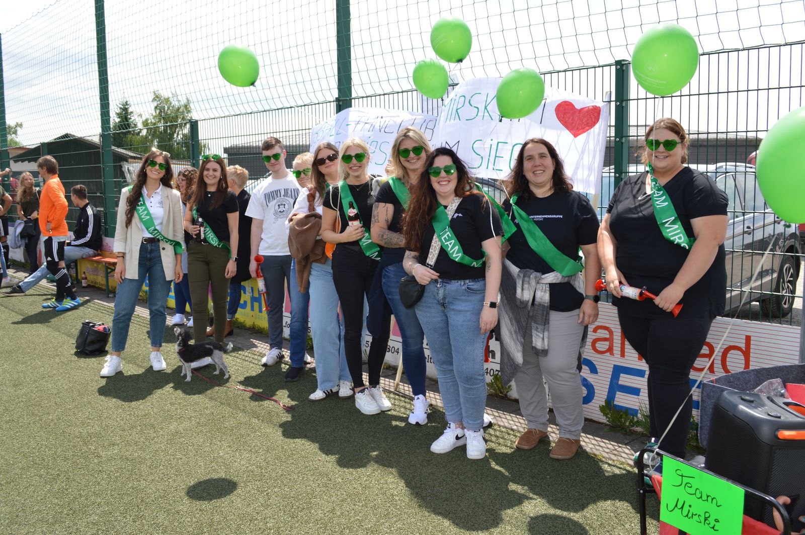 Fußballfans mit grünen Team-Schärpen und Luftballons feuern beim Firmenfußballturnier 2025 am Sportgelände des TV Freyung an.