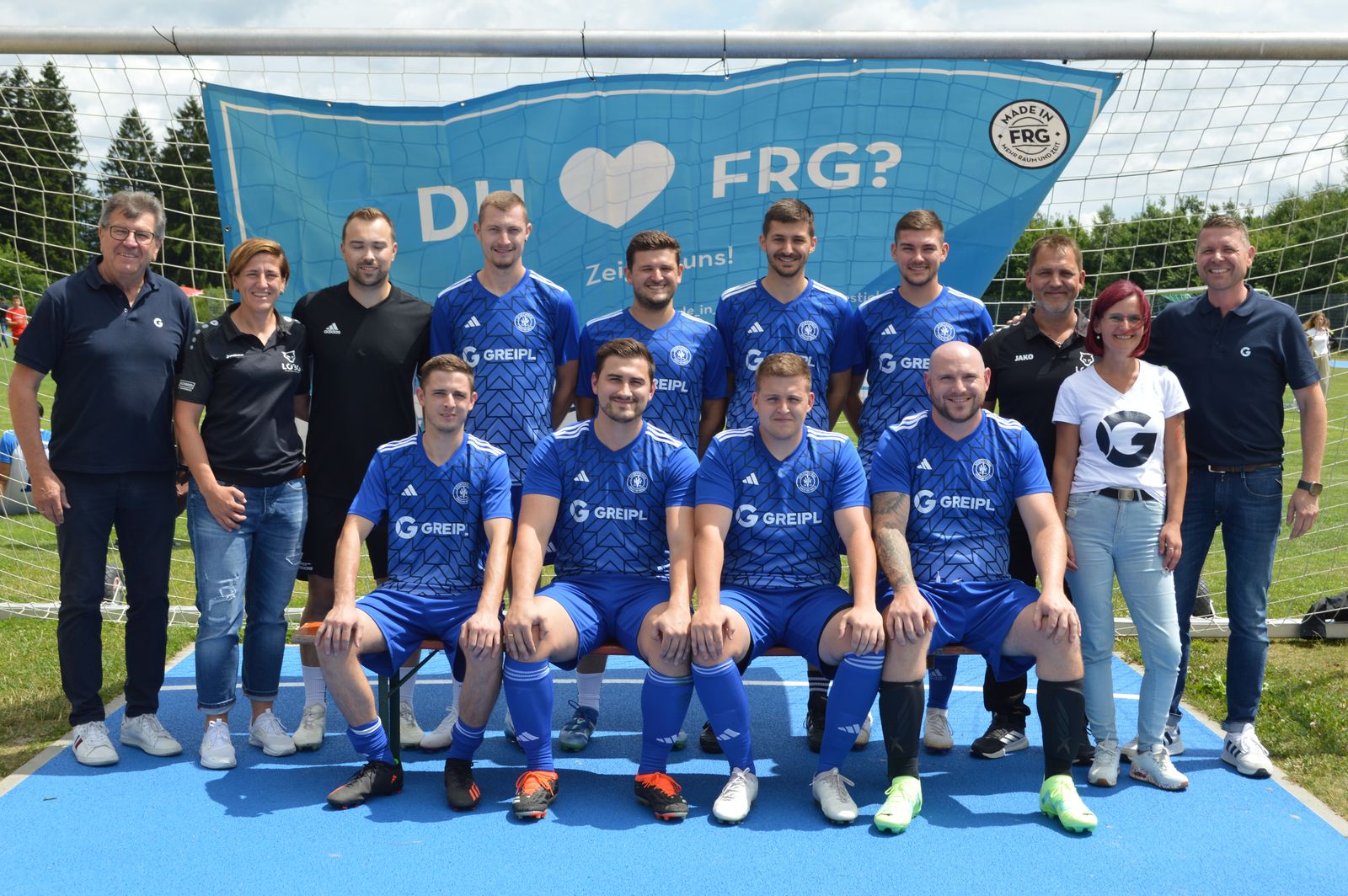 Eine Firmenfußballmannschaft in blauen Trikots posiert mit Begleitpersonen vor einem MADE in FRG-Banner beim Turnier in Freyung.