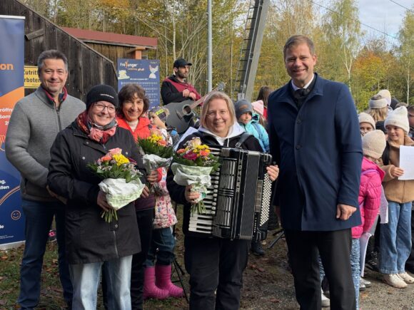 Beteiligte mit Blumen und eine Akkordeonspielerin feiern die Eröffnung des Freyunger Liederwegs mit Kindern am Geyersberg.
