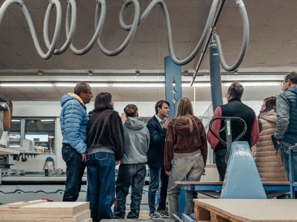 Bei der Langen Nacht der Wirtschaft verfolgen Besucher eine Führung durch eine Produktionshalle mit Maschinen und Absaugschläuchen.
