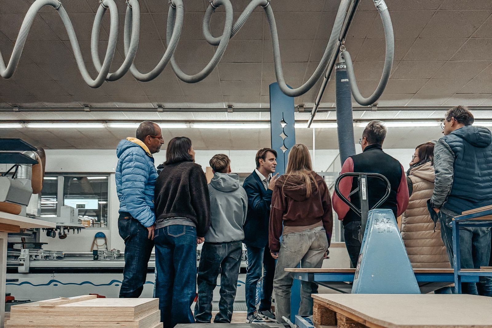 Bei der Langen Nacht der Wirtschaft verfolgen Besucher eine Führung durch eine Produktionshalle mit Maschinen und Absaugschläuchen.
