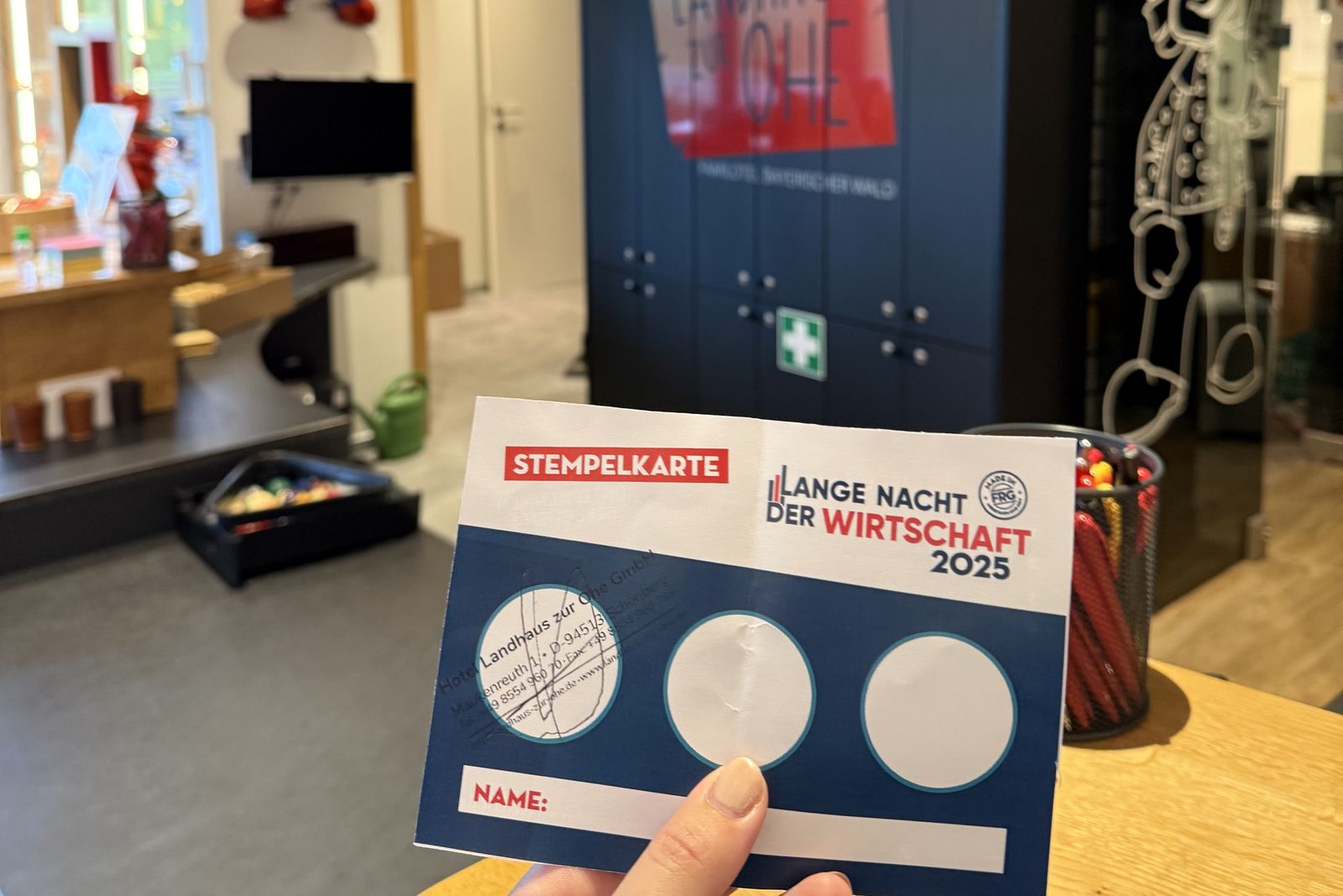 Eine Hand hält die Stempelkarte der Langen Nacht der Wirtschaft 2025 mit einem Unternehmensstempel und zwei freien Feldern.