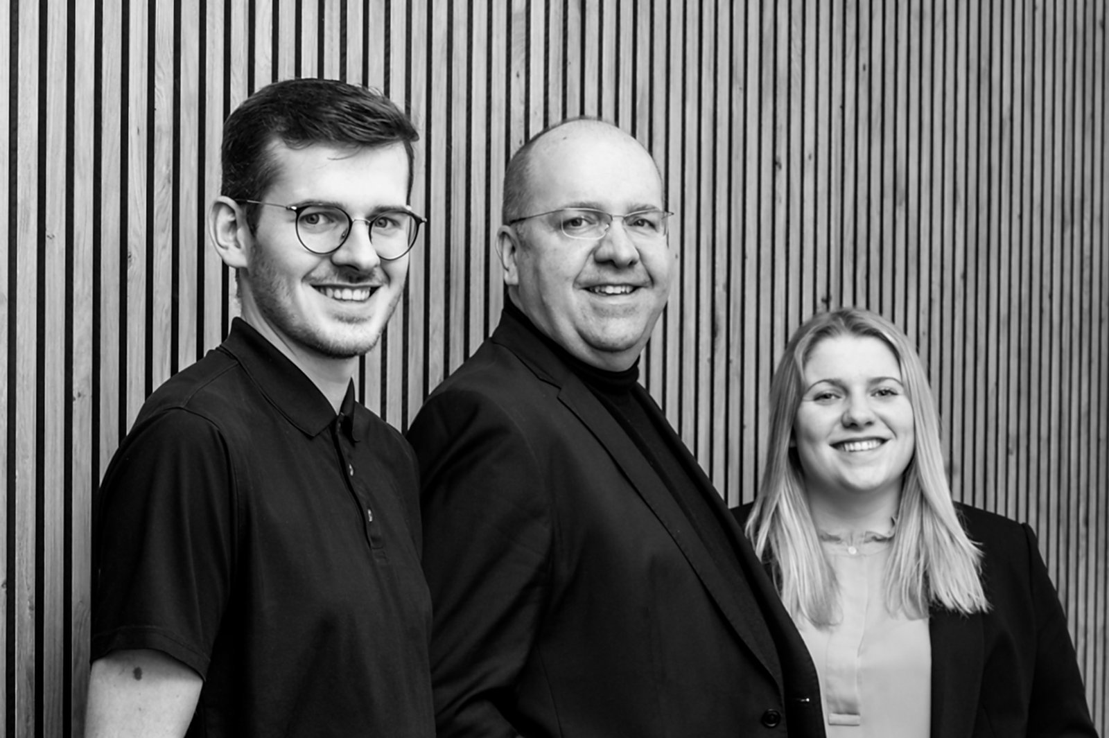 Drei lächelnde Mitglieder des SCHRAML.IT-Teams stehen vor einer Holzleistenwand; der IT-Dienstleister feiert 30 Jahre in Freyung.